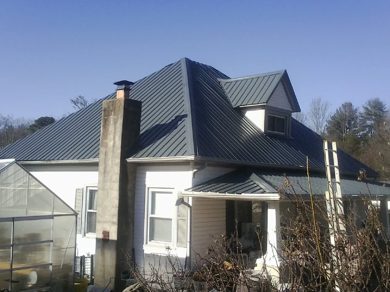 Dark blue standing seam metal roof on a white farmhouse with dormer — Slate & Tile Roof Repair by Roofing Brothers in Guys