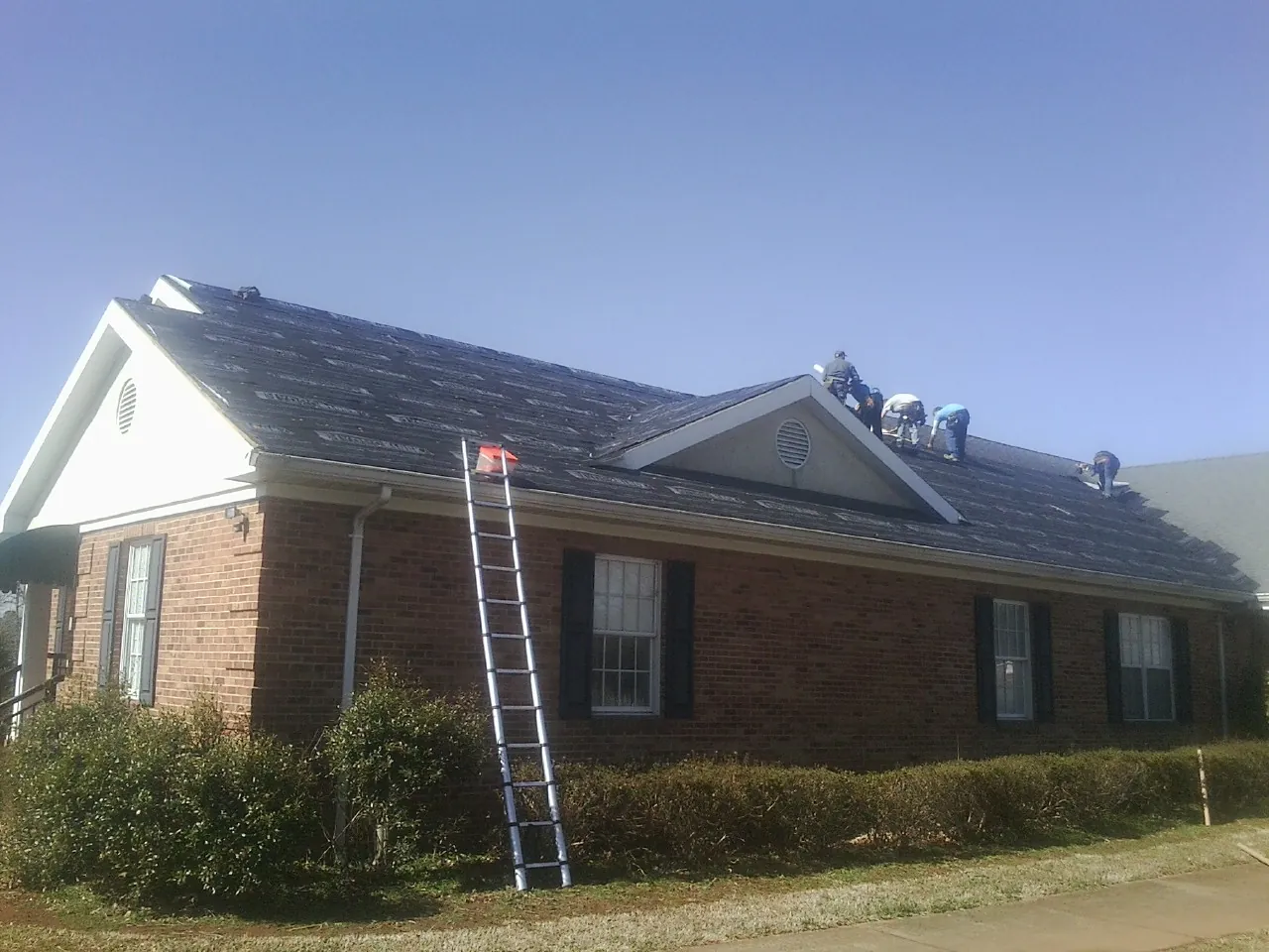 Crew tearing shingles off a brick ranch roof with a ladder set — Metal Roof Repair work by our crew in Guys