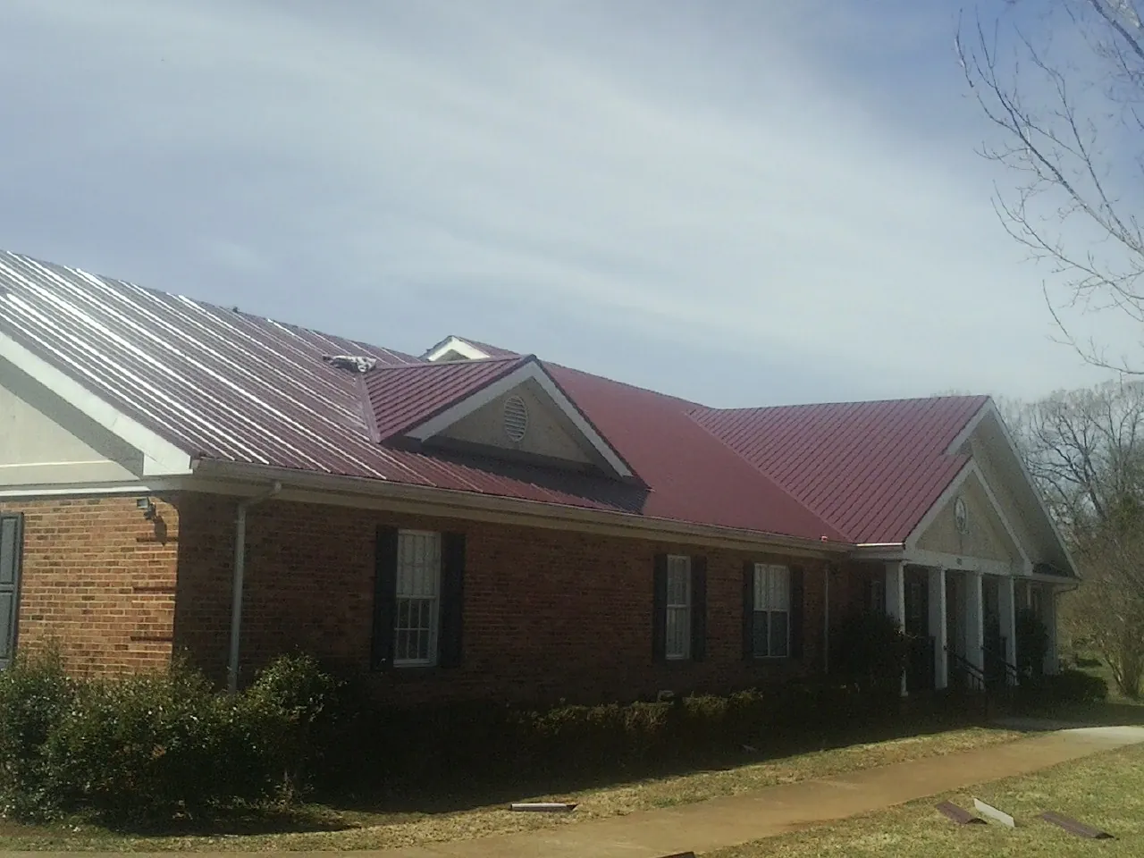 Red metal roof with gabled entries on a long brick building, from a Hail Damage Roof Repair job in Guys