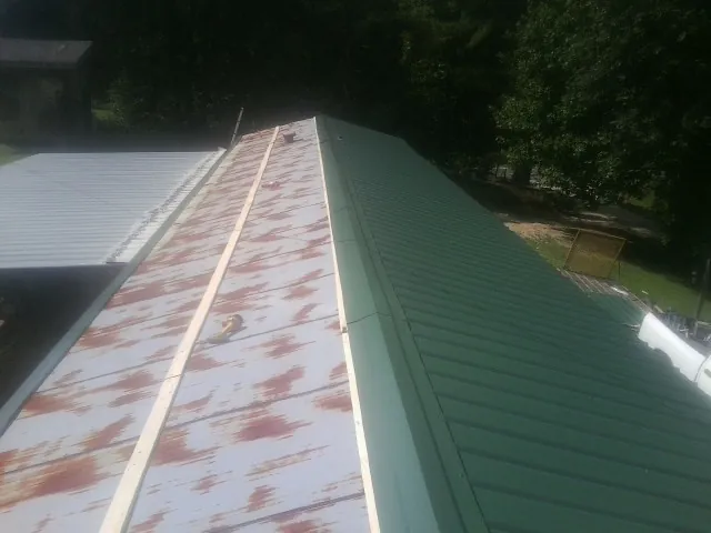 Old rusted panels beside newly installed green metal roofing — Wind Damage Roof Repair by Roofing Brothers in Guys