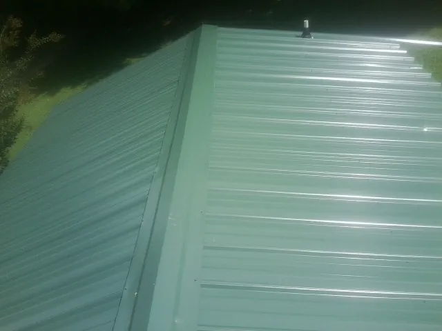 New green metal panels meeting at the ridge of a roof — Flat Roof Repair work by our crew in Guys