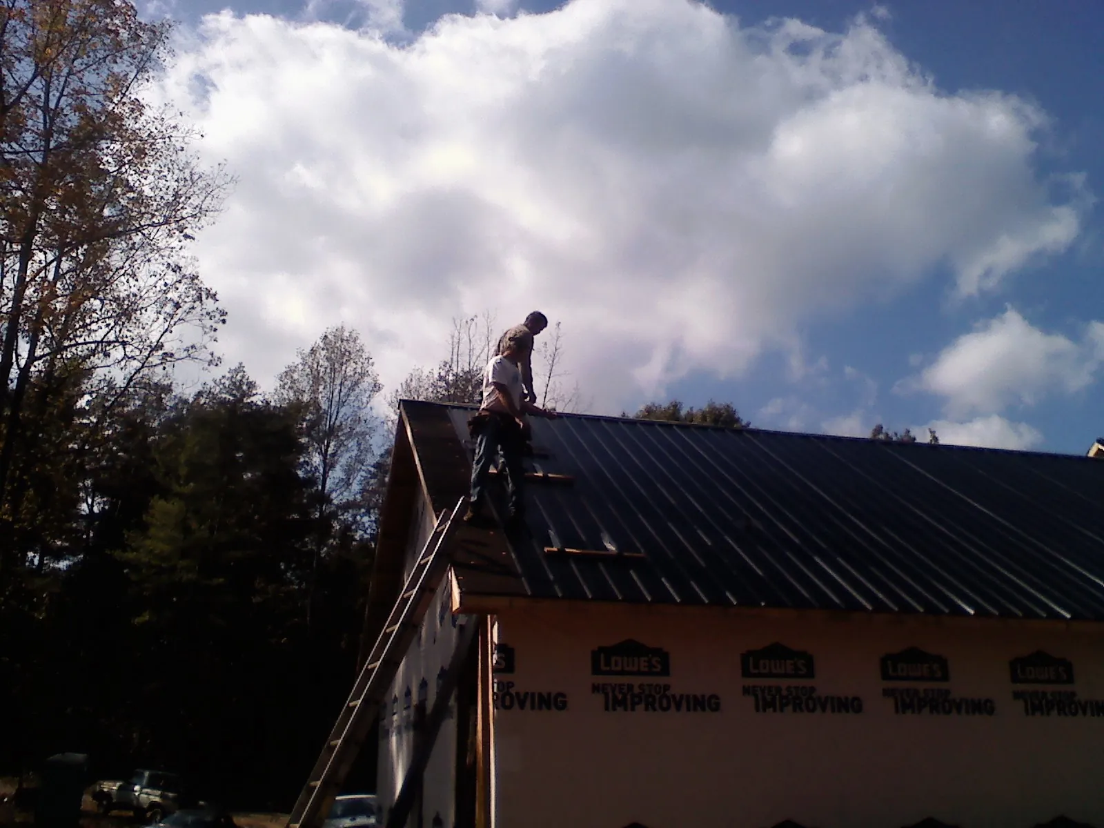 Roofer fastening dark metal panels high against a cloudy sky, from a Roof Inspection job in Guys