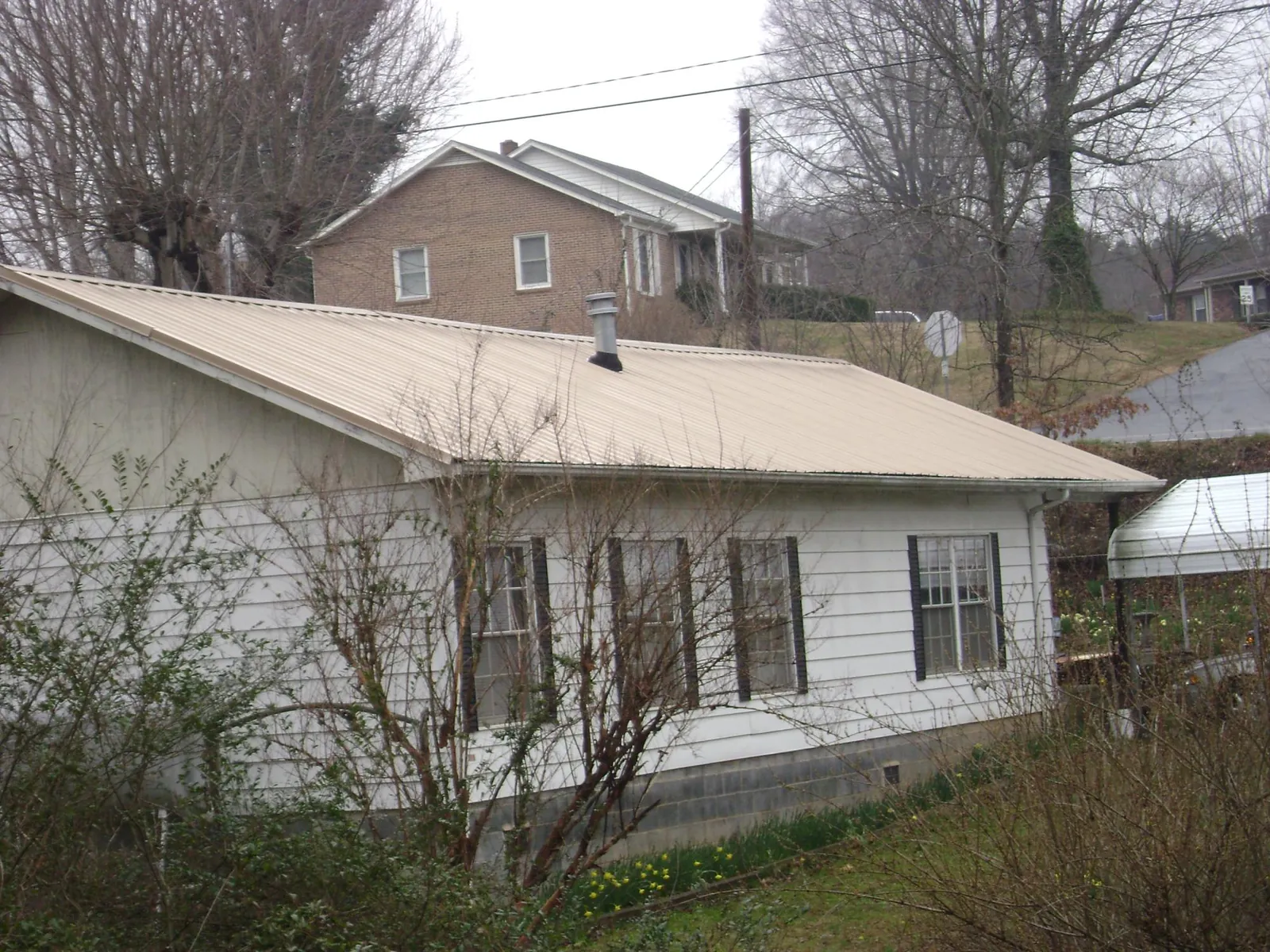 Tan metal roof on a white sided house set into a hillside — Commercial Roofing by Roofing Brothers in Guys