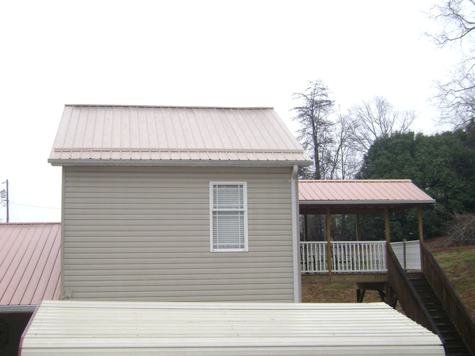 Tan metal roofs on a two story addition and attached porch, from a Roof Replacement job in Guys